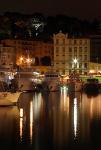 Sailboats moored on river by illuminated buildings in city at night