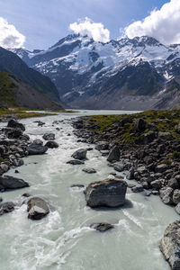 Scenic view of stream by snowcapped mountains against sky