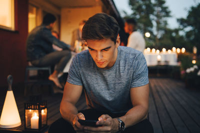 Young man using smart phone while friends in background during dinner party