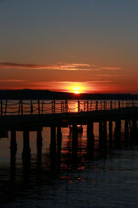 Silhouette pier over sea against sky during sunset