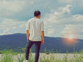 Rear view of man looking at field against sky