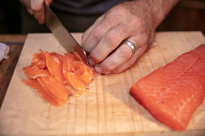 Cropped hands cutting salmon on cutting board