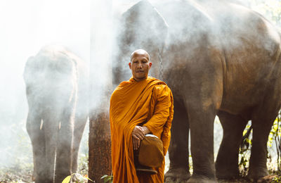 Portrait of monk standing against elephant in forest