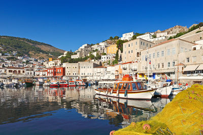 Sailboats moored in canal by town against clear blue sky