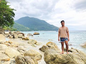 Full length of man standing on rock in sea against sky