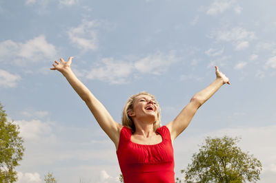 Happy woman with arms outstretched standing against sky