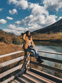 Beautiful young woman wearing autumn clothes, enjoying view of fall scenery by a lake