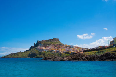 Buildings on mountain by sea against blue sky at castelsardo