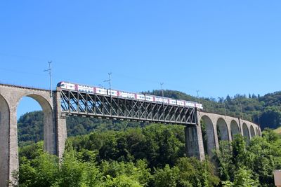 Low angle view of train moving on arch bridge against clear blue sky
