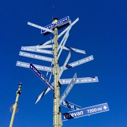 Low angle view of city directional sign against clear blue sky