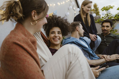 Smiling woman talking with female friends while sitting at party in balcony