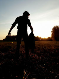 Silhouette man standing on field against sky during sunset