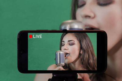 Close-up of smart phone filming woman signing against green background