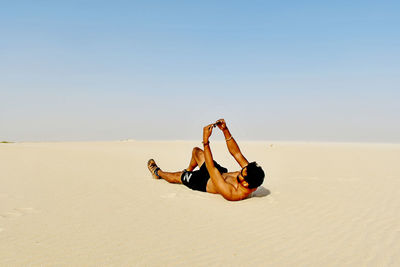 People relaxing on sand at beach against clear sky