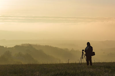 Silhouette man photographing on field against sky during sunset