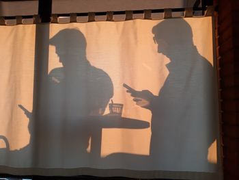 Shadow of men using mobile phone on curtain