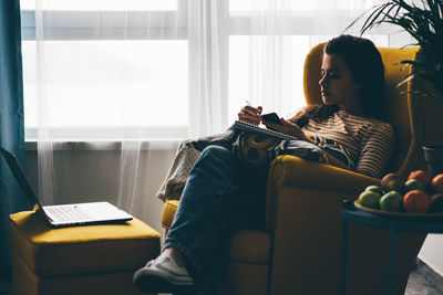 Young woman using laptop while sitting on sofa at home