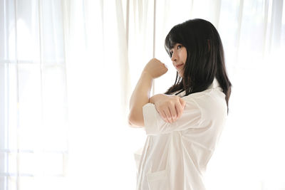 Side view of woman standing against curtain