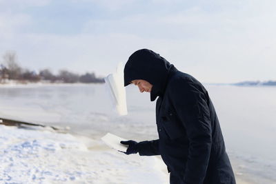 Side view of man standing by lake against sky during winter