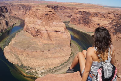 Rear view of woman with backpack sitting on rock formation at horseshoe bend