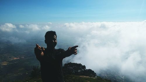 Man gesturing while standing on mountain against sky