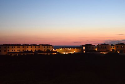 Illuminated buildings in city against clear sky at sunset