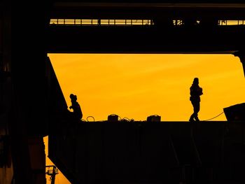 Silhouette man working against orange sky