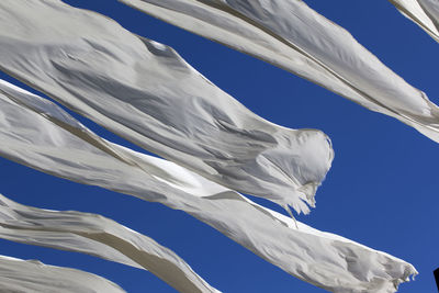 Low angle view of blowing white fabrics against blue sky