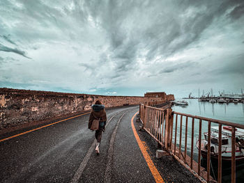 Rear view of man walking on road against sky