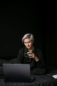 Woman working at home with laptop, drinking coffe, black colors interior