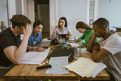 Young multiracial friends studying while doing homework at dining table