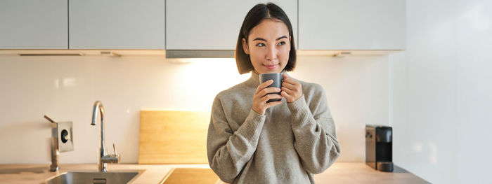 Portrait of young woman drinking water at home