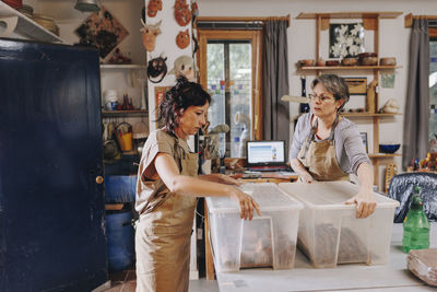 Entrepreneur with colleague holding plastic containers at ceramics workshop