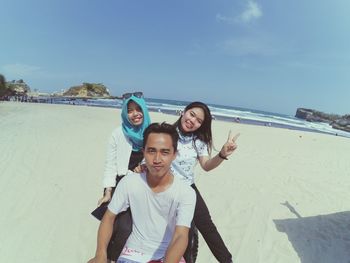 Portrait of happy friends on beach against sky