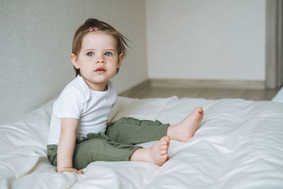 Cuty funny baby girl in home clothes sitting on bed at home