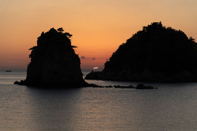 Rock formation in sea against romantic sky at sunset