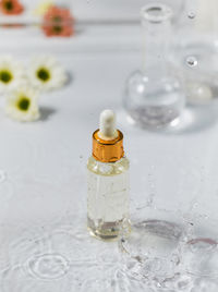 Glass dropper bottle with essential oil on wet table under falling down drops