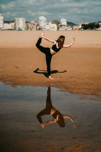 Side view of flexible unrecognizable female standing on sandy shore of river in natarajasana and practicing yoga while balancing on leg