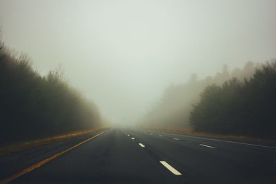 Road amidst trees against sky during foggy weather