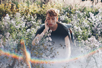 BEAUTIFUL YOUNG WOMAN WITH FLOWERS AGAINST PLANTS