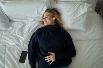 Woman listens to music with headphones in her bed in her apartment. mobile phone, technology.