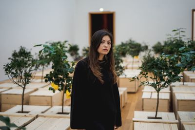 Portrait of young woman standing against potted plants