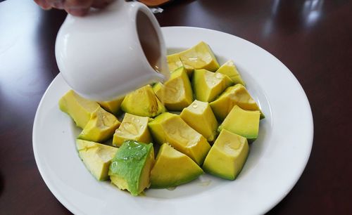 Close-up of jug pouring syrup on chopped avocados in plate at table