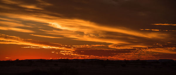 Silhouette landscape against dramatic sky during sunset