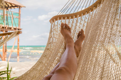 Low section of woman in hammock on beach against sky