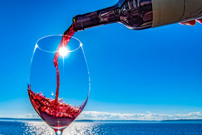 Close-up of person pouring wine in wine glass at sunny seaside