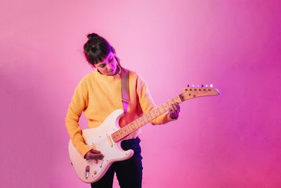Woman playing guitar against pink background