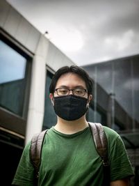 Portrait of young man standing against buildings and cloudy sky.