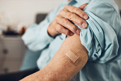 Senior man patient holding shirt sleeve up with a plaster in place of injection of vaccine