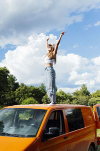 Side view of carefree female traveler standing on roof on van parked in nature in summer